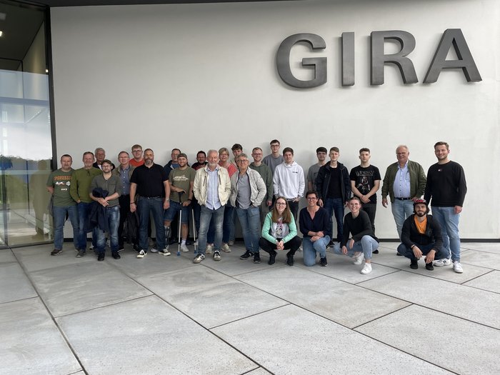 Eine Gruppe von Menschen steht vor einem modernen Gebäude mit dem Schriftzug 'GIRA' an der Wand, alle lächeln freundlich.