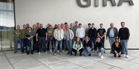 Eine Gruppe von Menschen steht vor einem modernen Gebäude mit dem Schriftzug 'GIRA' an der Wand, alle lächeln freundlich.