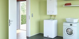 Ein heller Raum mit grünen Wänden, einer Waschmaschine und einem Wassertank, der an der Wand montiert ist.