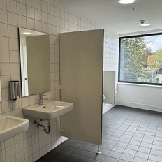 Helle, saubere Sanitäranlagen mit weißen Fliesen, zwei Waschbecken und einem Sichtfenster zur Außenlandschaft.