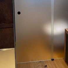 Die Dusche ist mit einer matten Glastür abgetrennt, während die Holzoberfläche der Kommode warm und einladend wirkt.