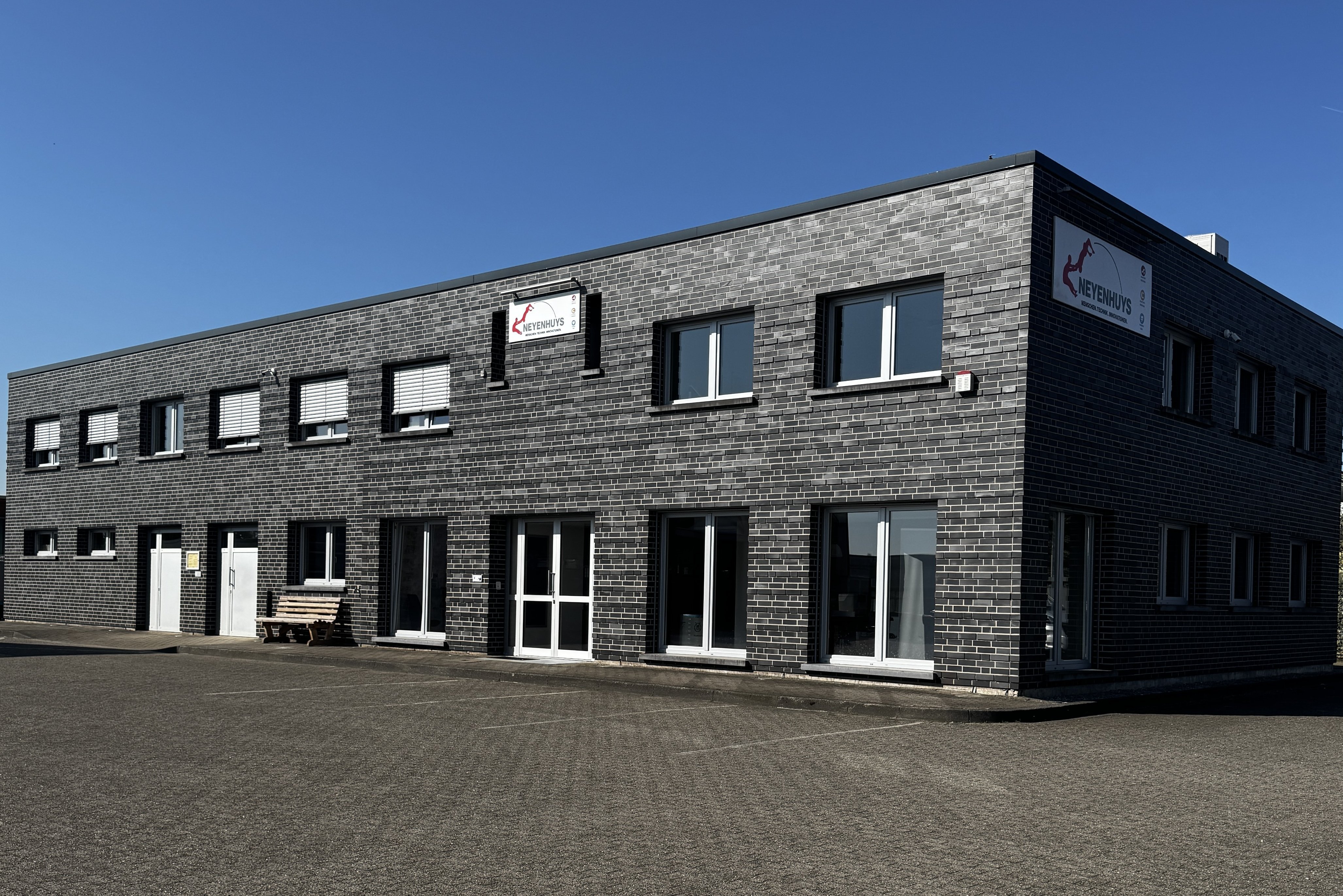 Ein modernes, zweigeschossiges Gebäude mit grauer Ziegelsteinfassade und großen Fenstern unter strahlend blauem Himmel.