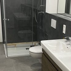 Der Raum zeigt eine stilvolle Dusche, einen weißen Toilettenbereich und eine große Spiegelwand über den Waschbecken.